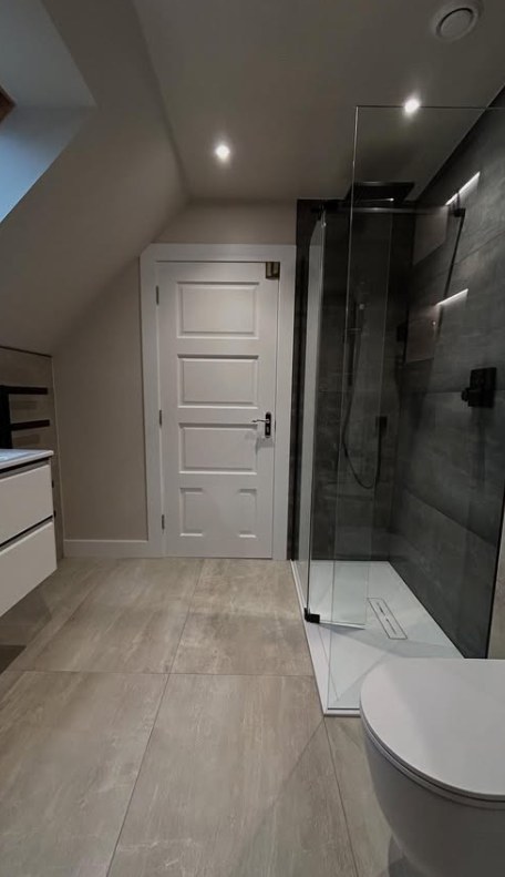 Attic en-suite with sloped ceiling, walk-in glass shower and light stone-effect tiles
