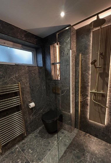 Dark marble shower with brushed gold fittings and backlit niches